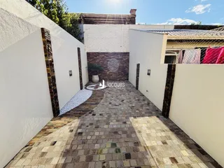 Vista de um pátio externo pavimentado com tijolos e paredes brancas.