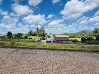 Vista externa de uma propriedade rural com vegetação e colinas ao fundo.