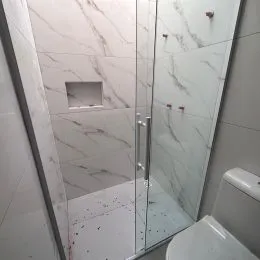 Foto de um banheiro com revestimento em mármore branco e box de vidro.