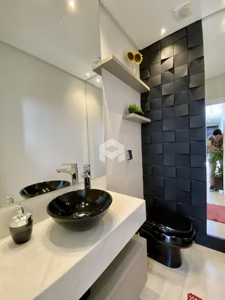Banheiro moderno com pias de apoio pretas e revestimento de parede em tijolinhos escuros.