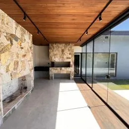 Ambiente interno com teto de madeira e parede de pedra, com vista para o exterior.