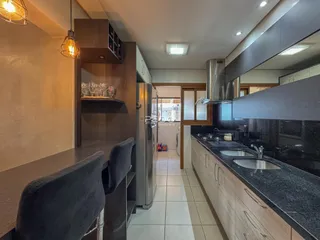 Vista interna de uma cozinha moderna com armários de madeira e bancadas escuras.