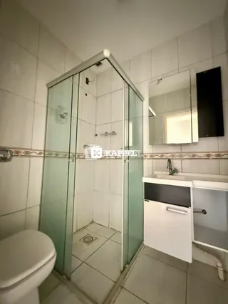 Banheiro com revestimento de azulejos brancos e box de vidro transparente.