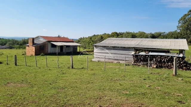 Vista externa de uma propriedade rural com estruturas de madeira em um campo gramado.