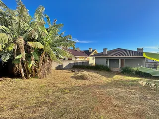 Vista da propriedade com vegetação seca no primeiro plano e uma residência ao fundo.