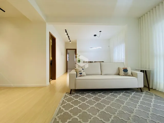 Sala de estar com sofá branco e piso de madeira clara.