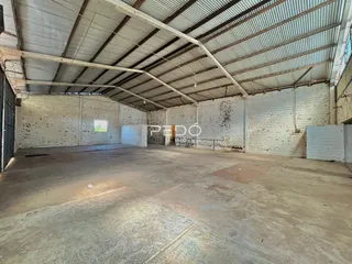 Imagem interna de um espaço industrial com estrutura de telhado metálico e piso de concreto.