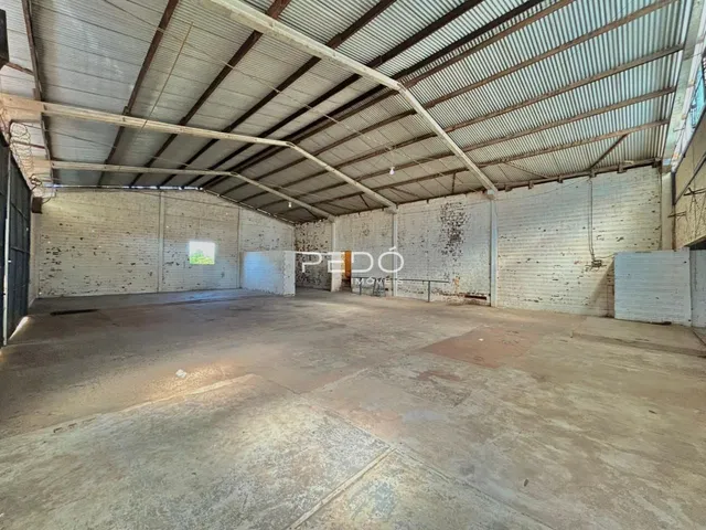 Imagem interna de um espaço industrial com estrutura de telhado metálico e piso de concreto.