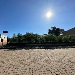 Vista externa de uma área pavimentada com árvores ao fundo.