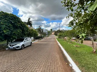 Vista externa da rua com vegetação e carro estacionado.