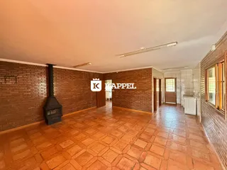 Uma foto interna mostra uma sala com piso de ladrilhos terrosos e paredes de tijolos aparentes.
