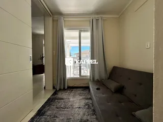 A sala de estar apresenta um sofá cinza e uma janela com cortinas.