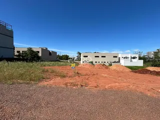 Vista externa de um terreno com vegetação e edifícios ao fundo.