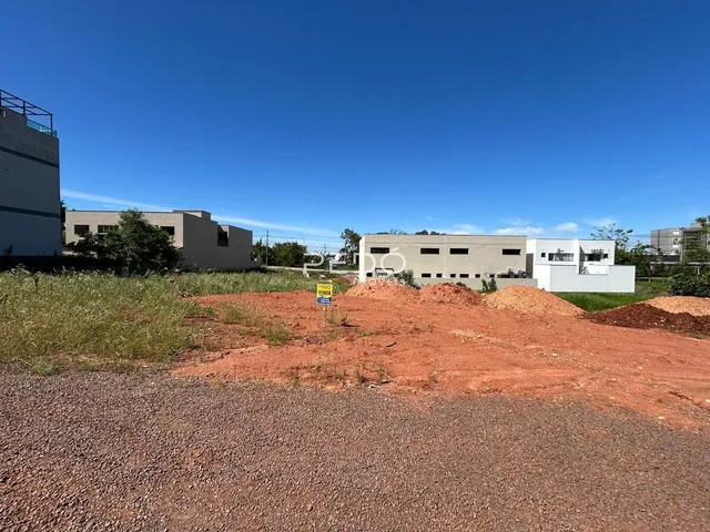 Vista externa de um terreno com vegetação e edifícios ao fundo.