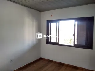 Ambiente interno com paredes brancas e piso de madeira, com uma grande janela.