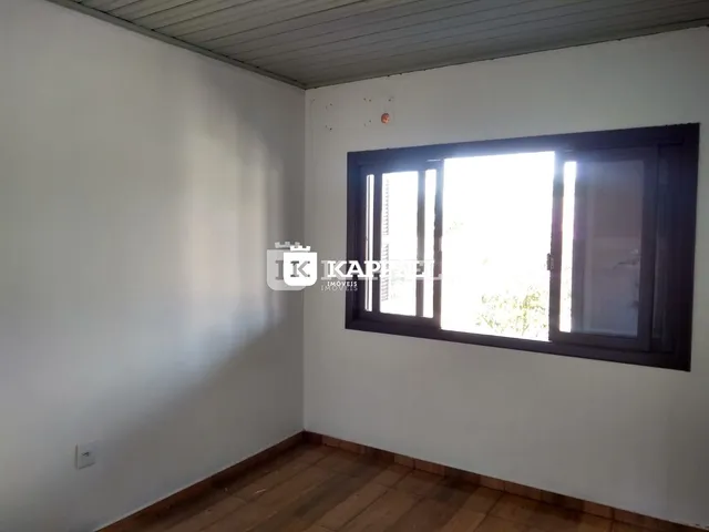 Ambiente interno com paredes brancas e piso de madeira, com uma grande janela.