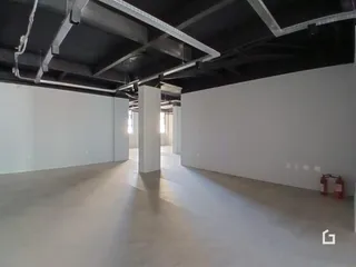 Corredor longo com estrutura de vigas exposta em ambiente interno.