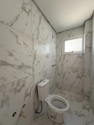 Um banheiro com paredes revestidas em mármore branco e um vaso sanitário branco.