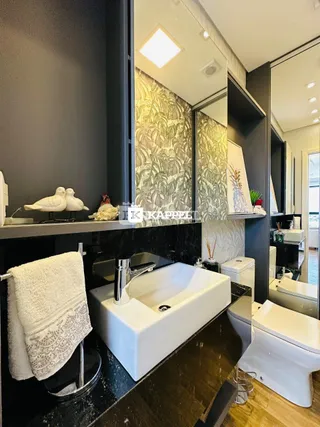 Banheiro com bancada escura e louças brancas.
