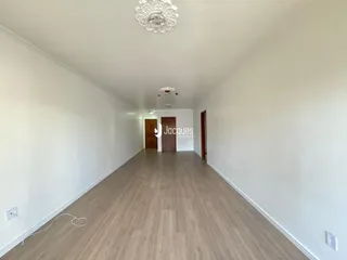Uma longa passagem interna com piso de madeira clara e paredes brancas.