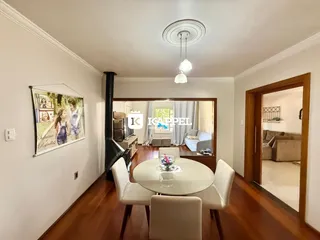 Sala de jantar com mesa redonda e cadeiras brancas em um ambiente com piso de madeira.