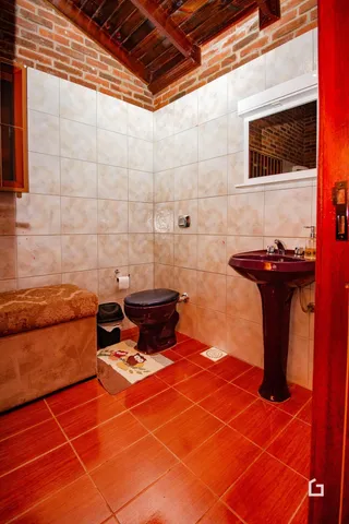 Foto de um banheiro com piso de cerâmica vermelha e paredes de tijolo aparente.