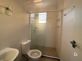 Foto interna de um banheiro com box de vidro e azulejos brancos.