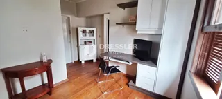 Interior de uma sala com piso de madeira e armários brancos.