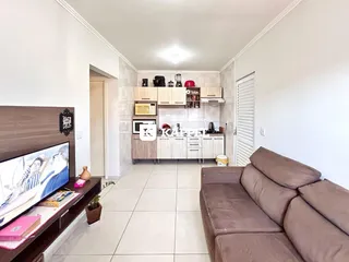Sala de estar com cozinha integrada e sofá de cor marrom.