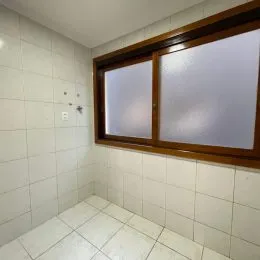 Vista interna de um corredor com paredes brancas e janela de madeira.