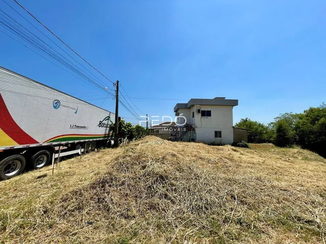 Vista externa de uma residência com terreno gramado e caminhão ao fundo.