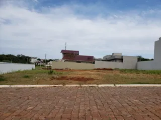 Vista externa de um terreno com grama seca e muro baixo.