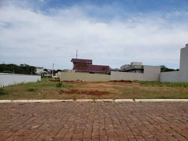 Vista externa de um terreno com grama seca e muro baixo.