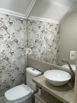 Foto de um banheiro com revestimento de parede floral e louças brancas.