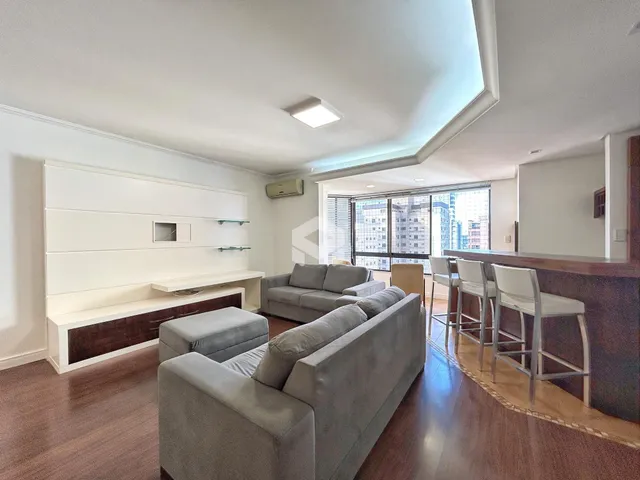 Sala de estar moderna com piso de madeira e grandes janelas.