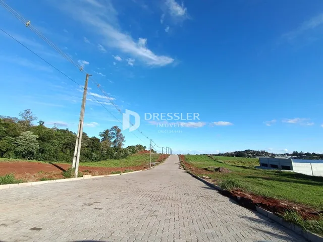Uma estrada pavimentada leva a um campo verde sob um céu azul.