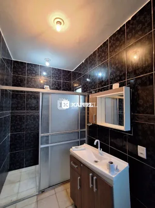 Foto de um banheiro com revestimento de azulejos escuros e bancada branca.