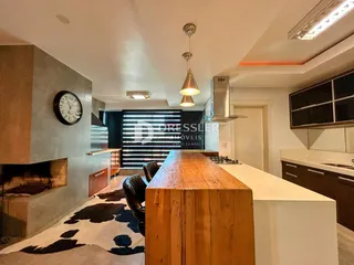 Interior de uma sala de estar com lareira e cozinha em um imóvel no Brasil.