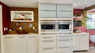 Vista interna de uma cozinha com armários brancos e painel de madeira.
