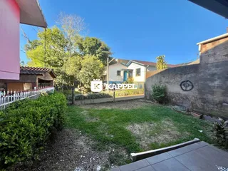 Vista externa do quintal com gramado e vegetação sob céu azul.