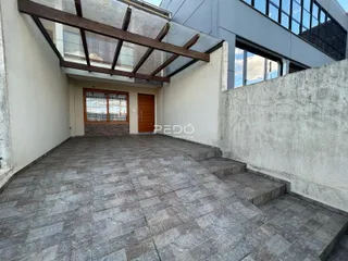 Área externa pavimentada com piso de lajes cinzas e parede de concreto.