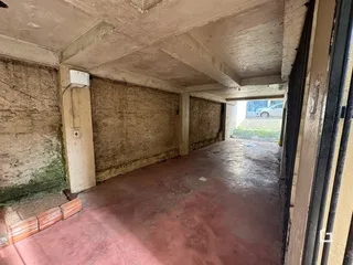Vista interna de um corredor com paredes de concreto aparente e piso de terra.