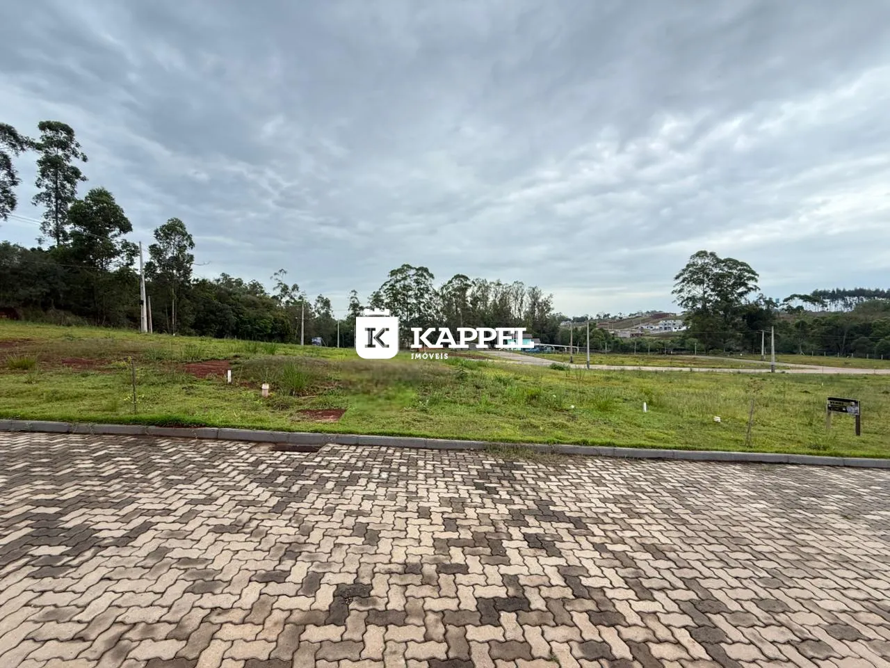 Vista externa de um terreno gramado com pavimentação de blocos.