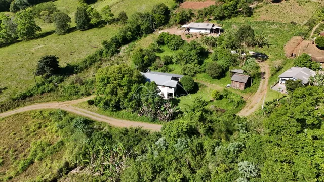 Vista aérea de uma propriedade rural em uma área verde e arborizada.