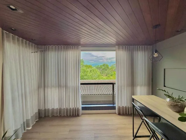Sala de estar com piso de madeira e cortinas brancas que dão vista para o exterior.