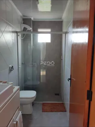 Interior de um banheiro com box de vidro e revestimento cerâmico branco.