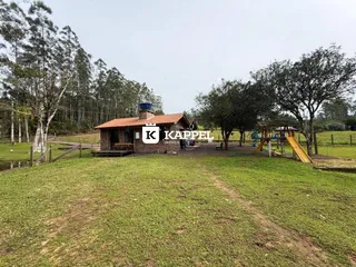 Exterior da casa de tijolos em uma propriedade rural com gramado e árvores.