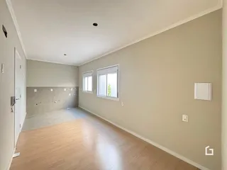 Ambiente interno de uma sala com piso de madeira clara e paredes bege.