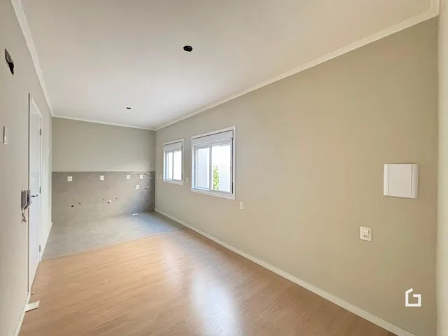 Ambiente interno de uma sala com piso de madeira clara e paredes bege.