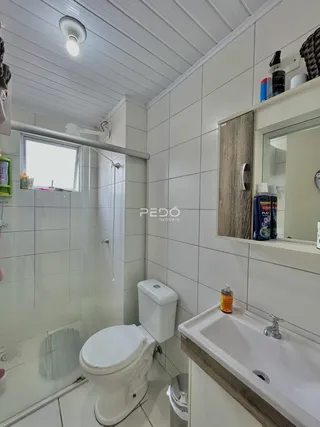 Banheiro com revestimento cerâmico branco e piso claro.